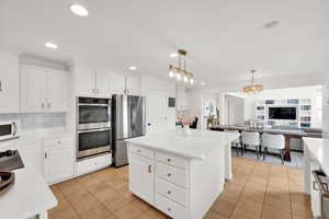 Kitchen featuring white cabinetry, stainless steel appliances, open floor plan, and light stone countertops