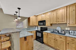 Kitchen with black appliances, a peninsula, light wood finish cabinets, and light stone countertops