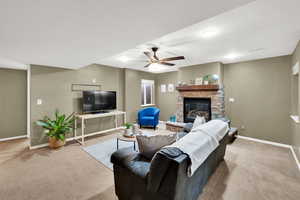 Living area featuring a ceiling fan, light carpet, and a fireplace