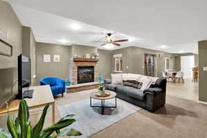 Carpeted living area featuring a ceiling fan and a stone fireplace