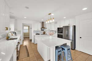 Kitchen featuring stainless steel appliances, a center island, white cabinets, and light stone countertops
