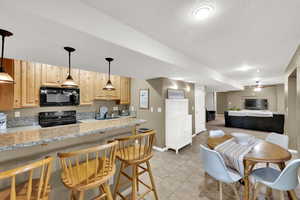 Kitchen with light wood finish cabinets, a kitchen bar, open floor plan, black appliances, and hanging light fixtures