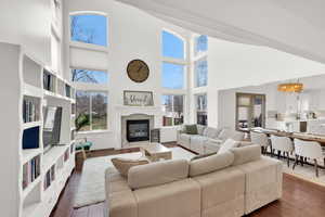 Living room with a high ceiling, dark wood-style floors, a tiled fireplace, and suspended lighting