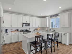 Kitchen featuring a kitchen bar, stainless steel appliances, quartz counter tops, white cabinetry, a kitchen island, and dark wood-style floors