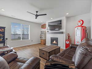 Living area with wood finished floors, a glass covered fireplace, ceiling fan, and recessed lighting