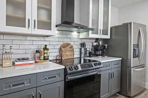 Kitchen with glass insert cabinets, gray cabinets, stainless steel appliances, light stone countertops, and decorative backsplash