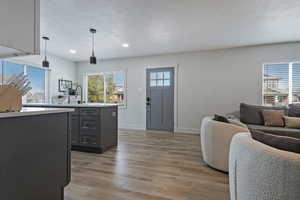Kitchen featuring a textured ceiling, open floor plan, light wood finished floors, gray cabinets, and hanging light fixtures