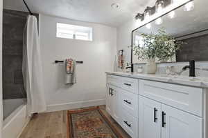 Full bath with double vanity, light wood-style flooring, and shower / bathtub combination with curtain