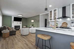 Kitchen with light stone countertops, a kitchen bar, light wood finished floors, backsplash, and a fireplace