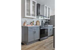 Two tone kitchen with glass fronted cabinets, light wood finished floors, stainless steel range with electric cooktop, two tone cabinetry, and tasteful backsplash