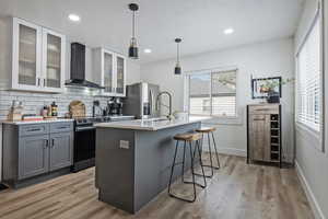 Dual tone kitchen with a kitchen bar, pendant lighting, two tone cabinetry, range with electric stovetop, and a center island with sink