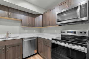 Kitchen with stainless steel appliances, dark wood finish cabinets, and light wood-style floors