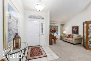 Entryway with light colored carpet, light tile patterned flooring, and vaulted ceiling
