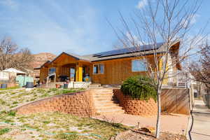 View of front of home with solar panels, a patio area, board and batten siding, and a shingled roof