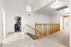Hallway with an upstairs landing, light tile patterned flooring, and a high ceiling