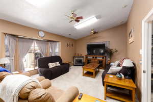 Carpeted living area featuring lofted ceiling, ceiling fan, and a fireplace