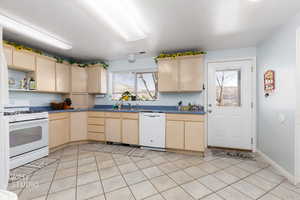 Kitchen with dark countertops, light wood finish cabinetry, white appliances, and plenty of natural light