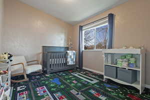 Bedroom featuring a nursery area, vaulted ceiling, a textured wall, and dark colored carpet