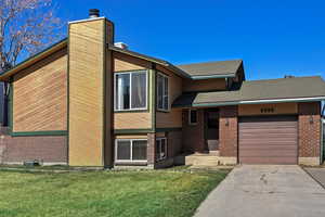View of front of property featuring an attached garage, a front yard, a chimney, concrete driveway, and a shingled roof