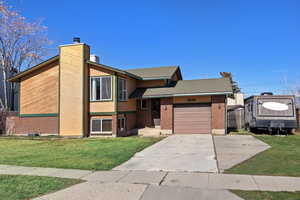 View of front of property featuring a chimney, driveway, brick siding, and an attached garage