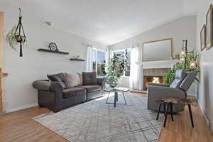 Living area featuring vaulted ceiling, light wood-style floors, and a tile fireplace