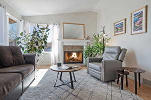 Living area with lofted ceiling, a tiled fireplace, and light wood-type flooring