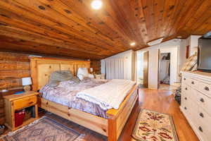 Bedroom featuring light wood-type flooring, rustic walls, and a vaulted wood ceiling