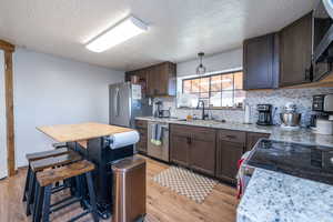 Kitchen featuring dark wood finish cabinetry, stainless steel appliances, decorative backsplash, light wood-style flooring, and a textured ceiling