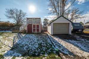 Snow covered garage with a garage, dirt driveway, and a storage shed