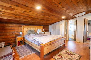Bedroom with light wood-style flooring, a vaulted wooden ceiling, log walls, ensuite bathroom, and recessed lighting