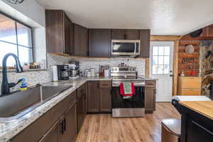 Kitchen with stainless steel appliances, dark wood finish cabinetry, light wood-style floors, a textured ceiling, and rustic walls