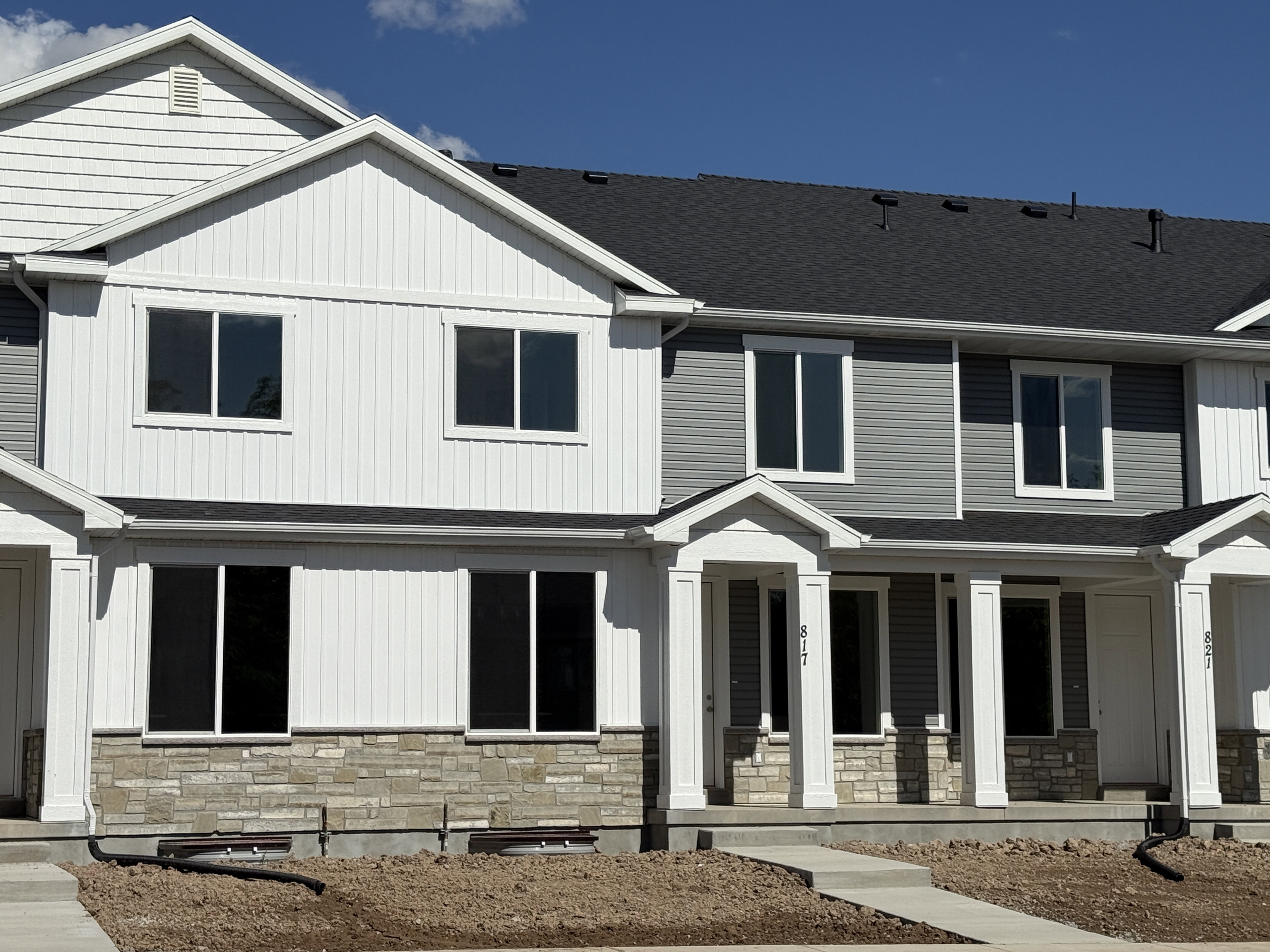 Multi-level townhome exterior featuring a combination of white vertical siding, grey horizontal siding, and a stacked stone facade