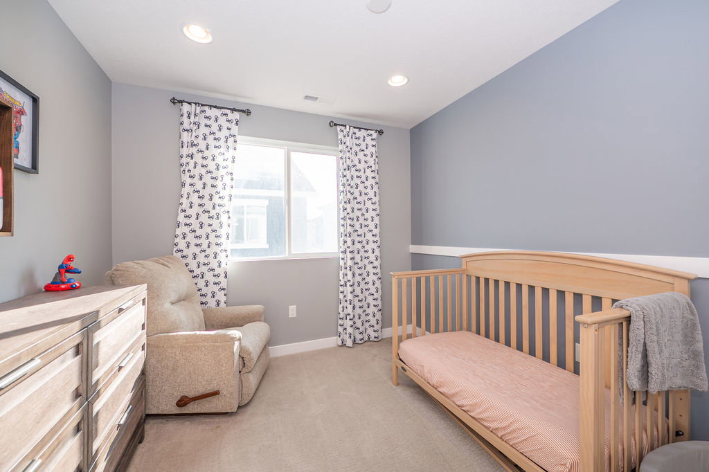 Bedroom with a crib, light colored carpet, and recessed lighting