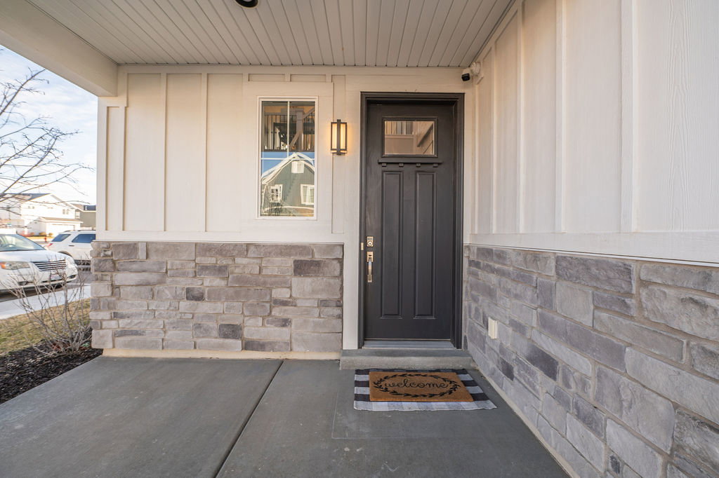 View of exterior entry with stone siding, board and batten siding, and covered porch