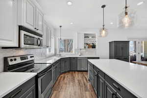Two tone kitchen with stainless steel appliances, dual tone cabinets, open shelves, dark wood-style floors, and light stone countertops