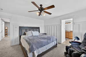 Bedroom featuring ceiling fan, connected bathroom, light carpet, wainscoting, and a decorative wall