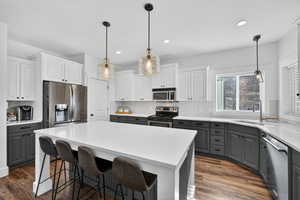 Kitchen featuring dual tone cabinetry, stainless steel appliances, light stone counters, a kitchen island, and dark wood-style flooring