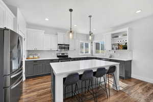 Two tone kitchen with dual tone cabinetry, stainless steel appliances, a center island, a kitchen bar, and open shelves