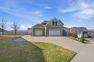 View of front of property with board and batten siding, driveway, a front lawn, roof with shingles, and a garage