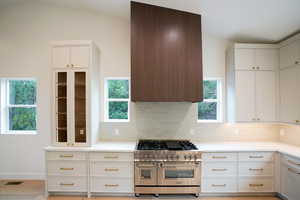 Kitchen with range with two ovens, white cabinetry, backsplash, and range hood