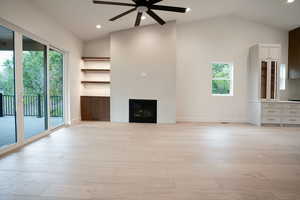 Unfurnished living room with ceiling fan, vaulted ceiling, a fireplace, light wood finished floors, and recessed lighting