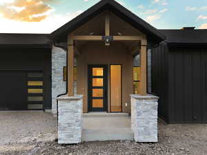Property entrance featuring stone siding, a porch, and an attached garage