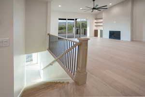 Stairs featuring wood-type flooring, recessed lighting, a glass covered fireplace, and ceiling fan