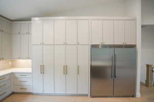 Kitchen with built in refrigerator, tasteful backsplash, light wood-type flooring, and light stone counters