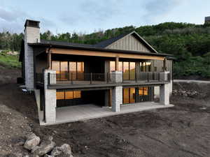 Back of property featuring board and batten siding, a chimney, a patio, and a forest view