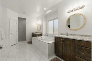Full bath featuring a garden tub, two vanities, light marble finish flooring, and recessed lighting