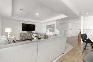 Living area featuring light wood finished floors, a raised ceiling, and recessed lighting