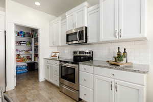 Kitchen featuring stainless steel appliances, white cabinets, light wood-style flooring, light stone countertops, and recessed lighting