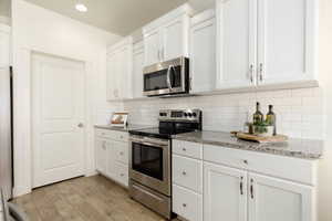 Kitchen featuring stainless steel appliances, white cabinets, light stone countertops, and recessed lighting