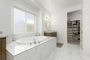 Bathroom with a garden tub, vanity, a spacious closet, and light marble finish flooring